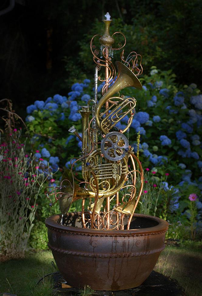 Musical instrument fountain sculpture consisting of copper tubing, a water wheel, upcycled french horns, flutes, trumpets, and brass and silver collectibles. 