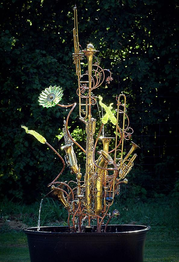 Musical instrument fountain sculpture constructed from copper tubing, a bicycle wheel, blown glass, repurposed brass and silver, and upcycled musical instruments including a trombone, tubas and trumpets.