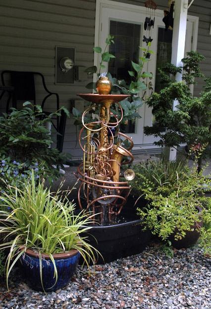 Musical instrument fountain sculpture consisting of copper tubing, a water wheel, brass and silver collectables, and upcycled musical instruments including saxes and trumpets.